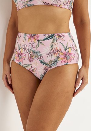 Højtaljede lyserøde bikini-bund med stort blomsterprint i nuancer af lyserød, fersken og grøn, båret af en stående person.