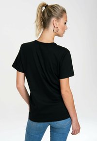 Black cotton t-shirt with short sleeves, crew neckline, relaxed fit, and smooth texture; worn with blue jeans, viewed from the back.