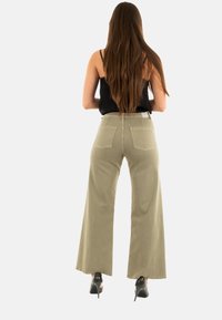 Pantaloni khaki a gamba larga con tasche posteriori cucite, vita alta e un fit casual. Indossati con tacchi neri e una maglia nera. Texture liscia.
