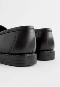Zapatos de cuero negro con un acabado suave, tacones redondeados y costuras detalladas a lo largo de los bordes. Suelas de goma con ranuras horizontales.