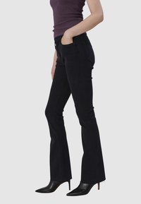 Jeans noirs évasés à taille mi-haute, avec des poches avant et arrière, et des coutures latérales. Associés à des escarpins noirs à talons aiguilles.