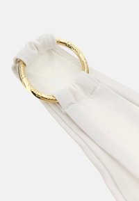 White fabric accessory with a textured finish, featuring a gold circular metal ring. The fabric is smoothly gathered around the ring.
