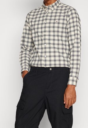 Karierte Button-Up-Hemd in Creme und Marine, mit klassischem Kragen und subtiler Logo. Kombiniert mit schwarzen Cargo-Hosen, die Taschen zeigen.