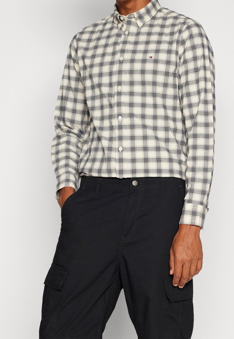 Camicia a quadri in crema e blu navy, con colletto classico e logo discreto. Abbinata a pantaloni cargo neri con tasche.