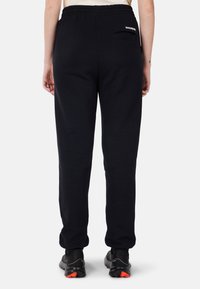 Zwarte, slim-fit trainingsbroeken met een elastische tailleband, details op de achterzak en een zachte textuur. Gekocht met zwarte sportschoenen met rode accenten.