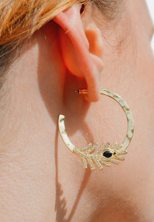 Goldene Creolen mit strukturiertem Finish, versehen mit einem Handdesign, das mit klaren Rhinsteinen und einem zentralen schwarzen Stein geschmückt ist.