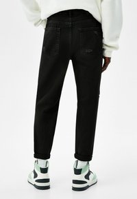 Černé denimové kalhoty se volným střihem, vybavené zadními kapsami a viditelnými švy. Kombinovány s vysokými teniskami v bílé barvě se zelenými akcenty.