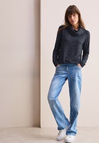 Maglione a collo alto grigio scuro a maniche lunghe, abbinato a jeans a gamba dritta blu chiaro e sneakers bianche. Tessuto morbido con vestibilità comoda.