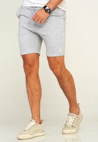 Gray cotton blend shorts with elastic waistband, drawstring, side pockets, and white logo detail. Paired with beige suede sneakers.