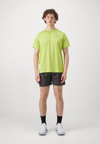Men's athletic outfit featuring a bright green short-sleeve t-shirt and dark shorts. Includes white sneakers and black socks. Simple design.