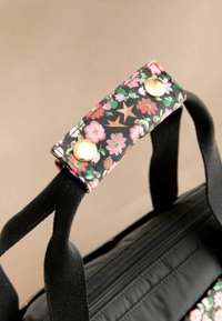 Bloemrijke zwarte stoffen tasriem met gouden drukknoopjes, versierd met levendige roze en groene bloemen. Zwarte handgrepen met een gestructureerd patroon.