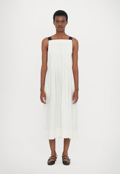 Abito midi bianco plissettato con spalline nere, caratterizzato da un scollo dritto e un tessuto fluido. Abbinato a delle ballerine nere.