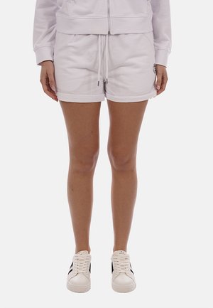 Persona che indossa pantaloncini con coulisse di colore chiaro, una giacca con zip abbinata e sneakers bianche con strisce nere.