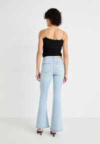 Svart strikket topp med tynne sølvkjede-stropper, kombinert med lyseblå, utsvingte jeans med høy midje og baklommer.