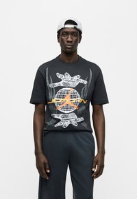 Μαύρο μπλουζάκι με κοντά μανίκια που διαθέτει γραφικό τύπωμα με χέρια και ένα παγκόσμιο χάρτη σε λευκό και πορτοκαλί, με ομαλή υφή και άνετη εφαρμογή.