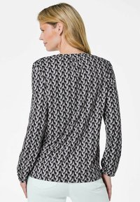 Blusa a maniche lunghe con un motivo geometrico in bianco e nero, realizzata in tessuto leggero con scollatura rotonda e delicate arricciature sul retro.