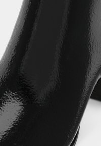 Must mustankäsi saapad, millel on sile, peegeldav pind ja kitsenev disain. Omab ümarat varvast ja diskreetset kontsa.