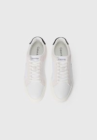 Witte sneakers met lichte suede accenten, ronde neus, witte veters, Calvin Klein-logo op de binnenzool en een zwarte hieltab.