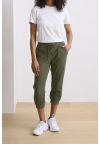 Olijfgroene cropped broeken met een broekband met trekkoord, aansluitende boorden en een relaxte pasvorm, gecombineerd met een eenvoudig wit T-shirt en witte sneakers.