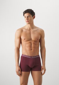 Bordeauxfarbene Boxershorts aus weichem Stoff mit glatter Textur, ausgestattet mit einem kontrastierenden, markierten Taillenbund.