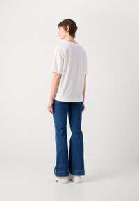 Vit bomullströja med korta ärmar, tillsammans med utsvängda blå denimjeans. Har en enkel design, avslappnad passform och enhetliga färger.