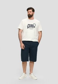 T-shirt blanc à manches courtes avec un graphique "PURE JUICE", associé à un short bleu marine jusqu'aux genoux. Les chaussures sont des baskets blanches.