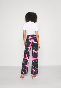 Calças largas com um tecido preto apresentando um padrão de relâmpago rosa. Combinadas com uma blusa justa branca e sandálias de salto rosa.