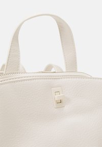 Bolso de cuero blanco con textura suave, asas dobles, cierre de cremallera y detalle de broche rectangular en el frente.