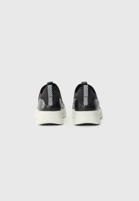 Black knit sneakers with a smooth black heel, white sole, and striped pull tabs. Features a textured surface and modern design.