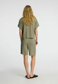 Olive green two-piece outfit featuring a loose-fitting short-sleeve top and knee-length shorts, made from a textured fabric, paired with black slip-on shoes.