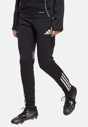 Zwarte sportieve broek met witte zijstrepen, AeroReady merkbranding en een reflecterende patch, gecombineerd met zwarte voetbalschoenen.