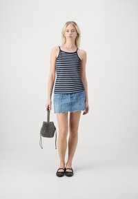 Navy and white striped tank top paired with a light blue denim mini skirt, featuring frayed hem. Black studded flats and a textured bag.