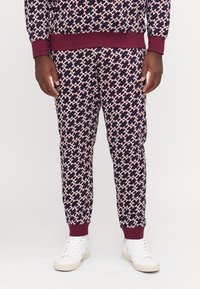 Geprinte joggingbroeken van bordeauxstof, met een geometrisch patroon in marineblauw, wit en rood. Geribbelde boorden en tailleband. Witte sneakers.