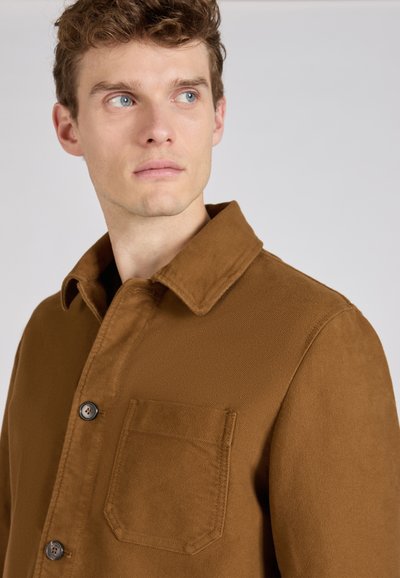 Brązowa kurtka koszulowa wykonana z miękkiego materiału, z zapięciem na guziki, kołnierzykiem typu pointed oraz kieszenią na piersi. Gładka tekstura w jednolitym kolorze.