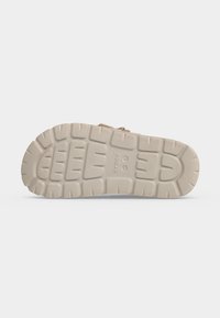 Semelle beige de sandale Crocs vue de dessous, montrant des rainures texturées et le nom de la marque "crocs" en relief au centre.