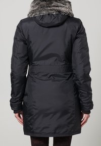 Svart vadderad parkas med huva som har en fuskpälskrage, markerad midja och slät textur, som når till mitten av låret.