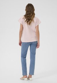 Haut rose clair à manches courtes avec des détails en dentelle aux épaules associé à un jean droit bleu clair et des sandales à talons blanches.