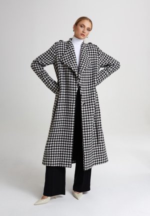 Czarny i biały płaszcz o wzorze houndstooth z kołnierzem szalowym, otwarty z przodu, z długimi rękawami, w połączeniu z czarnymi spodniami i kremowymi klasycznymi szpilkami.