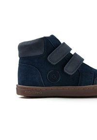 Zapatilla alta de ante azul marino con dos correas de Velcro, un logotipo circular en el costado y una suela de goma marrón.