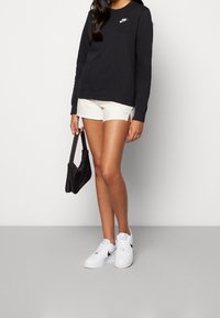 Czarny sweatshirt Nike, kremowe szorty, białe sneakersy Nike oraz czarna torebka. Zawiera ikoniczne logo na sweatshirtcie oraz rozcięcia po bokach szortów.