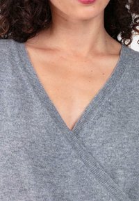 Pull en maille gris à enfiler avec un col en V profond, présentant des bords côtelés et une texture douce. Aucun motif ni détail métallique visible.