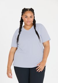 Lys grå kortærmet V-hals T-shirt lavet af glat stof, med en afslappet pasform. Bæret med mørkfargede bukser, der fremhæver toppen.