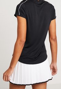 Persona che indossa un top nero a maniche corte con piping bianco e una gonna plissè bianca con orlo nero, vista da dietro.