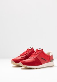 Baskets rouges en cuir et daim, avec un design texturé, une fermeture à lacets et une semelle de couleur crème avec des détails de marque subtils.