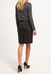 Gonna a matita nera con una silhouette aderente e uno spacco sul retro, abbinata a un top grigio a maniche lunghe cropped, indossata con scarpe nere con tacco alto.