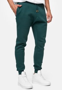 Dark teal joggers in soft cotton blend, featuring an elastic waistband with drawstrings, side pockets, and ribbed ankle cuffs.