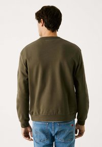 Olivgrön bomullströja med långa ärmar, ribbad krage och nederkant, enkel design och varumärkeslogotyp på nackens baksida. Matchad med blåjeans.