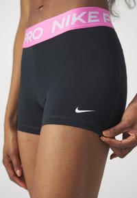 Crne atletske kratke hlače s ružičastim Nike Pro pojasom, s bijelim Nike swoosh logotipom sa strane i glatkom, rastezljivom tkaninom.