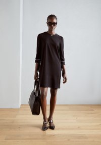 Black dress with three-quarter sleeves and white trim, paired with a structured black handbag and pointed toe black heels with gold accents.