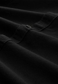 Tela negra con una textura suave; presenta pliegues y un cierre de botón. El material parece elástico y duradero con sutiles detalles de costura.